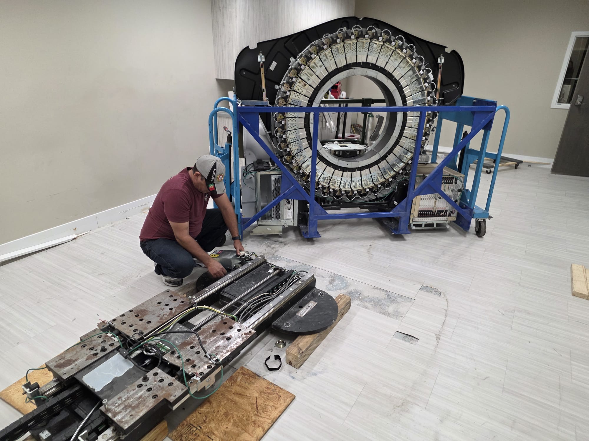 Technician working alongside a PET detector ring and patient table during service.